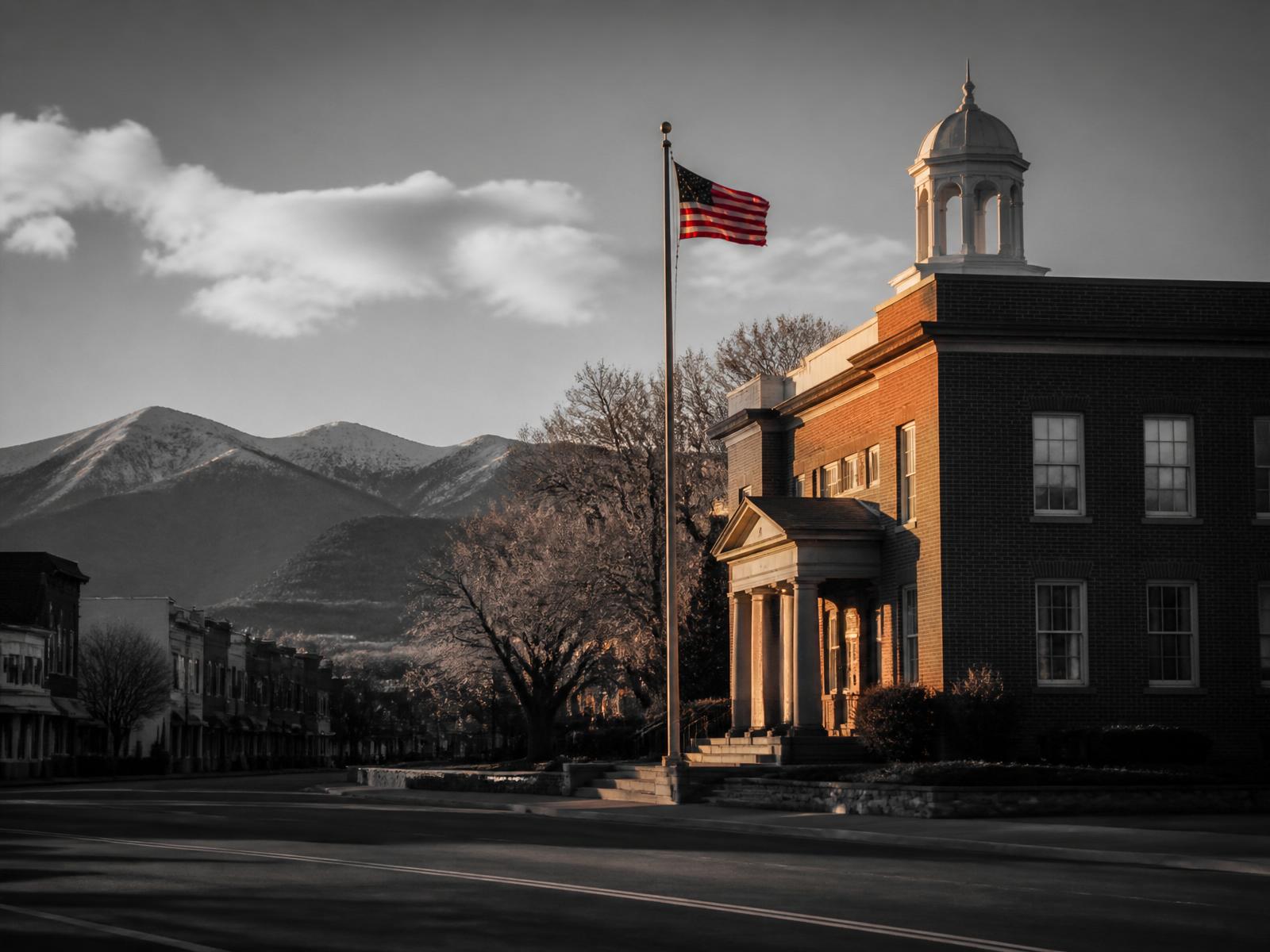 Historic small-town civic building at golden hour with mountains in the background.